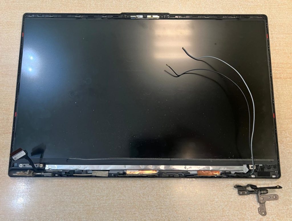 Módulo de pantalla desmontado con la pieza metálica de la bisagra desprendida de su soporte.