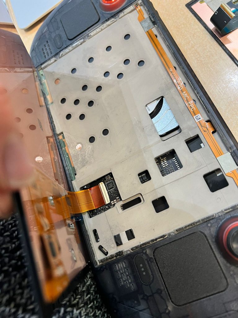 Macro de la conexión del cable flexible (flex) naranja de la pantalla a la placa base de la Steam Deck OLED dentro del blindaje metálico.