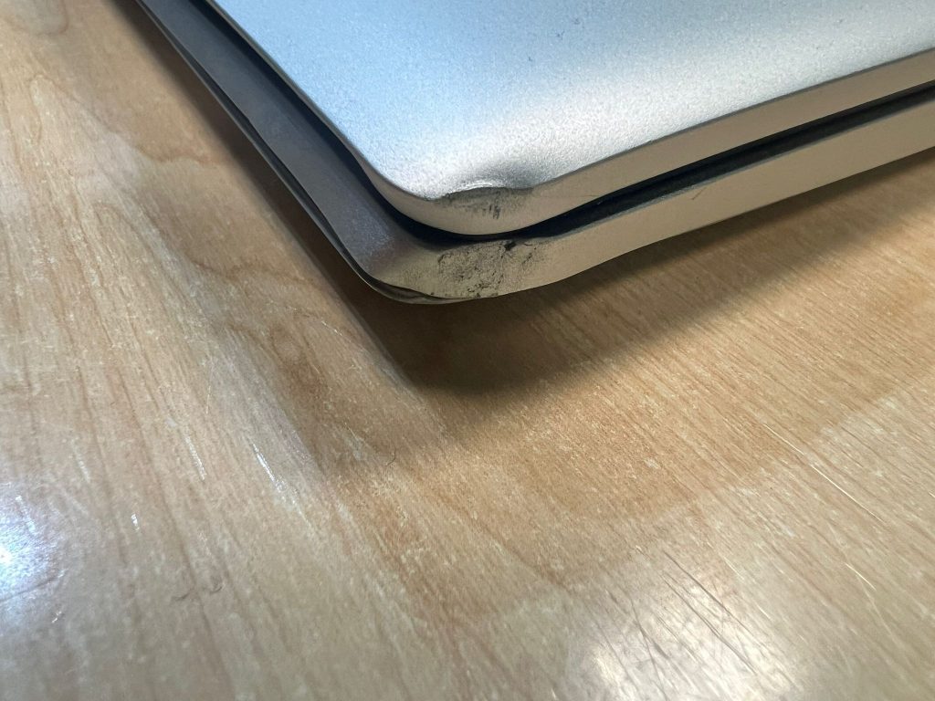 Detalle del chasis de aluminio deformado por caída en esquina de laptop HP.