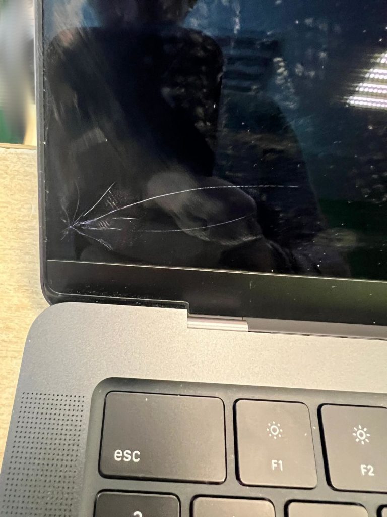 Primer plano de grietas por impacto en la esquina inferior de una pantalla MacBook Pro.