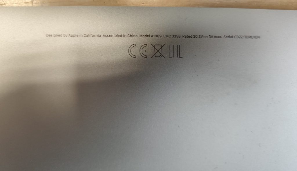 Detalle de la tapa trasera del portátil confirmando el modelo MacBook Pro A1989 y número de serie.