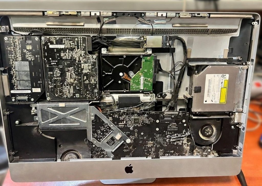 Vista interna de un iMac de 27 pulgadas desmontado, mostrando la fuente de alimentación, disco duro y ventiladores durante la reparación.