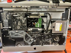 Vista interna de un iMac de 27 pulgadas desmontado, mostrando la fuente de alimentación, disco duro y ventiladores durante la reparación.