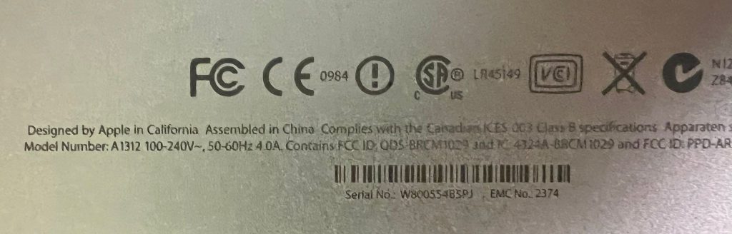 Detalle de la etiqueta trasera de un iMac 27 pulgadas modelo A1312 con número de serie y especificaciones técnicas.