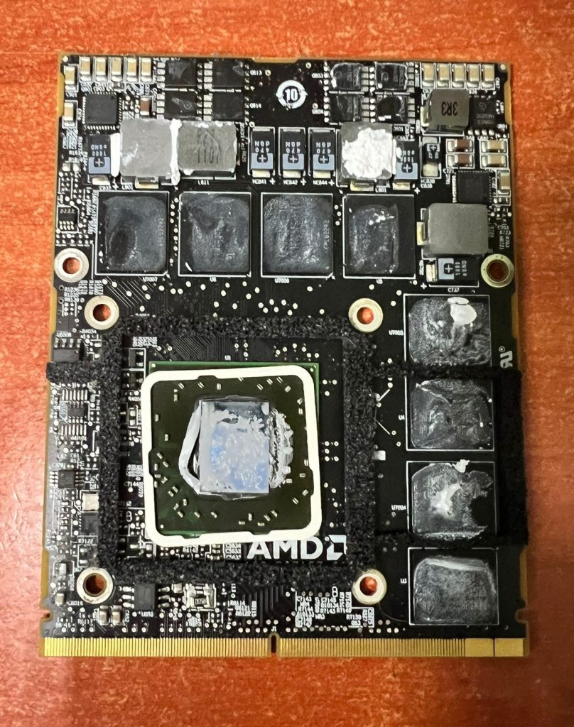 Tarjeta gráfica AMD tipo MXM de un iMac A1312 desmontada con restos de pasta térmica antes de ser reparada.