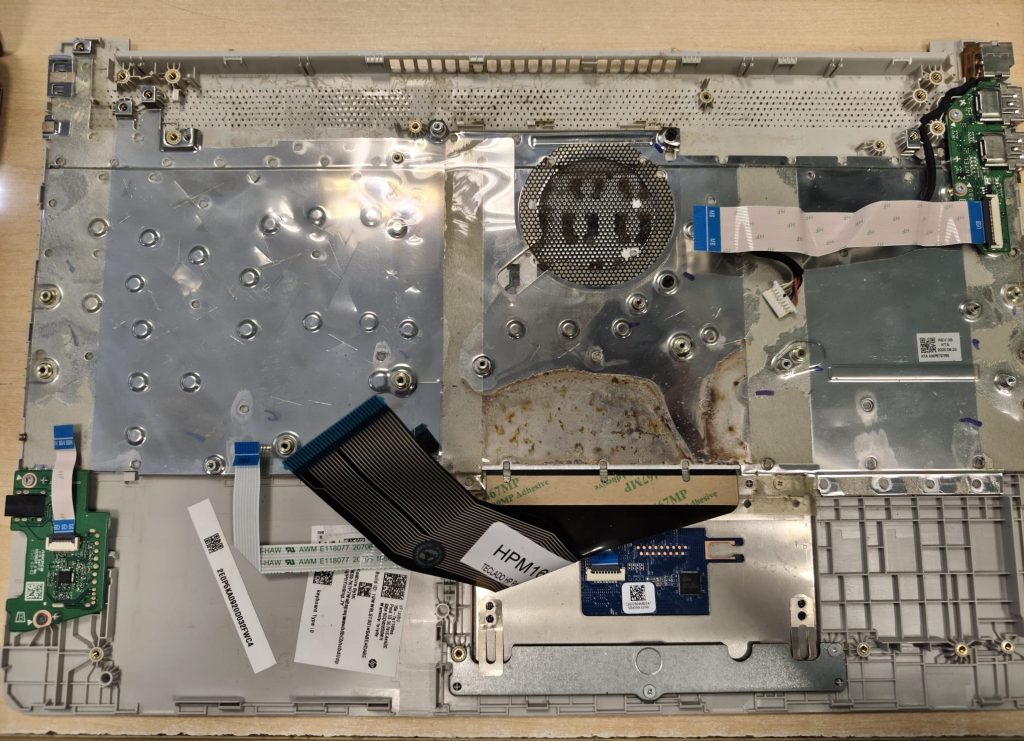 Interior del chasis de HP 15s mostrando restos de corrosión y humedad bajo el teclado.