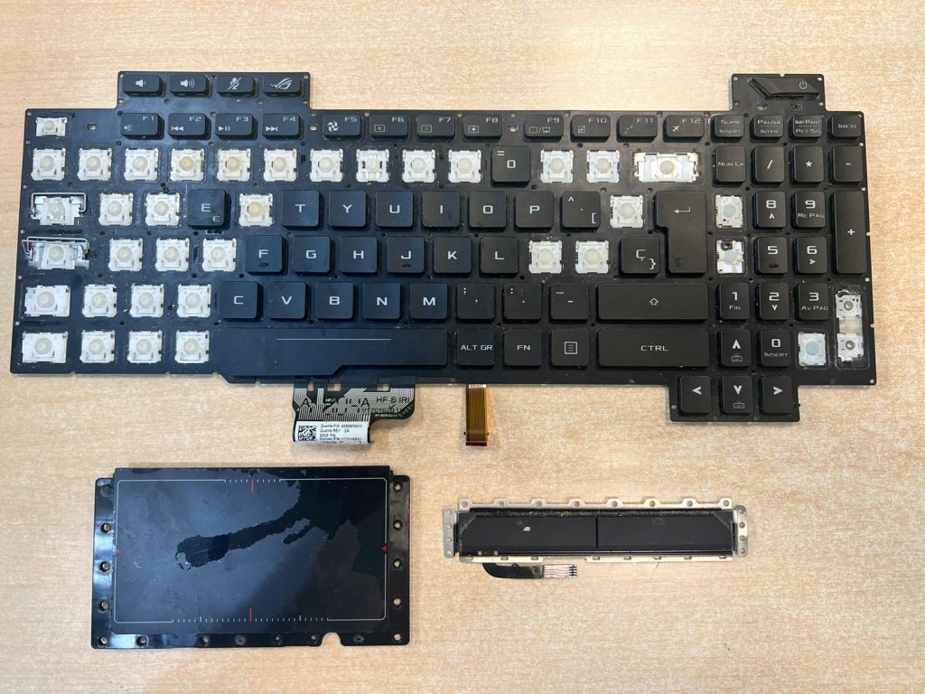 Componentes internos extraídos: teclado dañado con teclas faltantes y módulo de touchpad del Asus GL703.