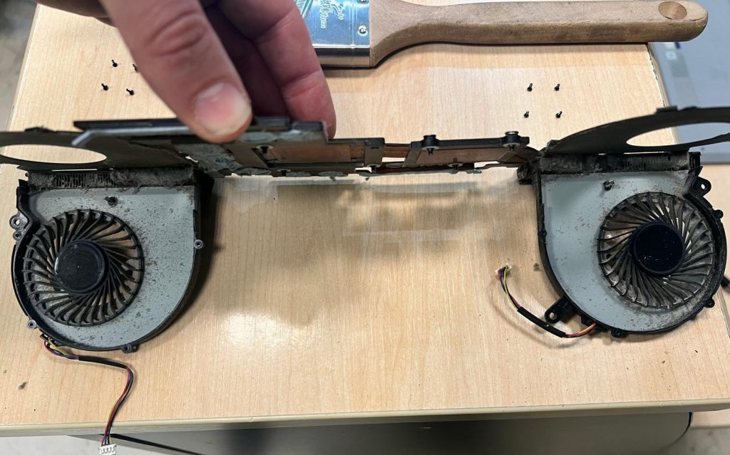 Ventiladores y heatpipes de cobre desmontados con obstrucciones de polvo en las salidas de aire.