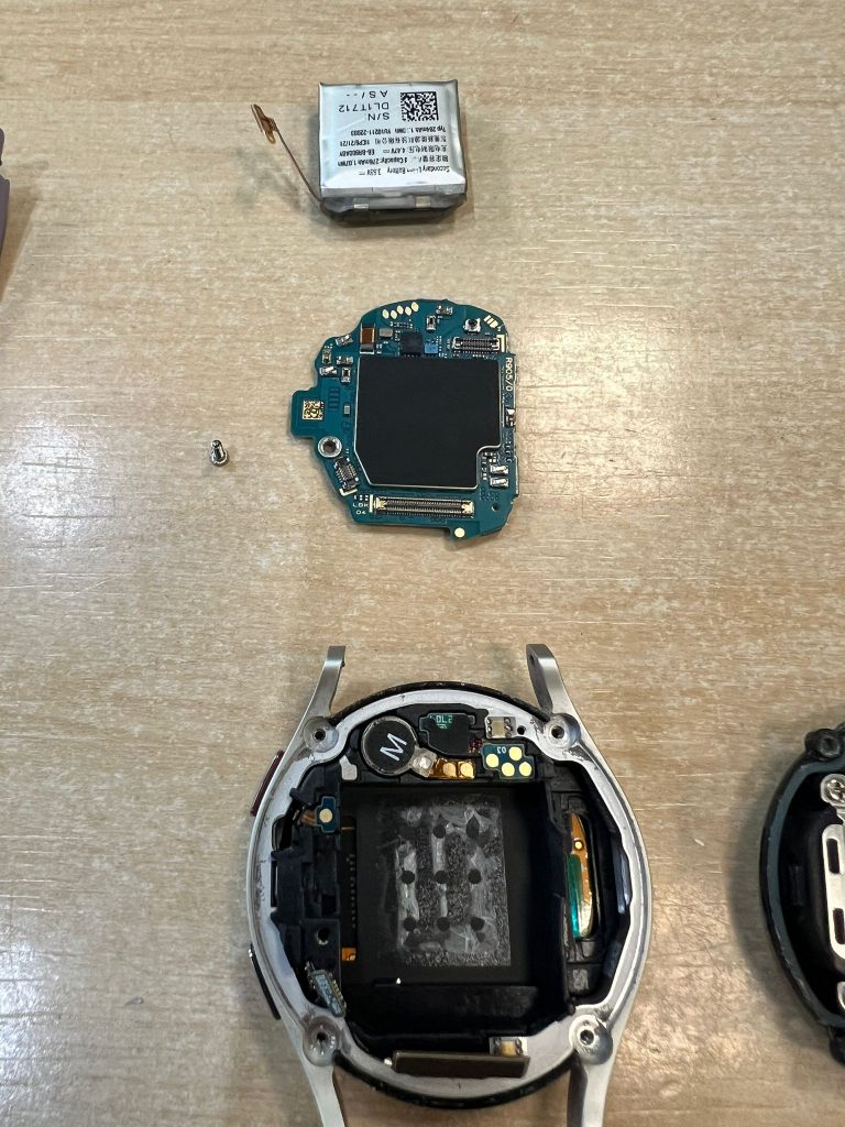 Despiece del Samsung Watch 5 incluyendo batería extraída, placa lógica y chasis del reloj.