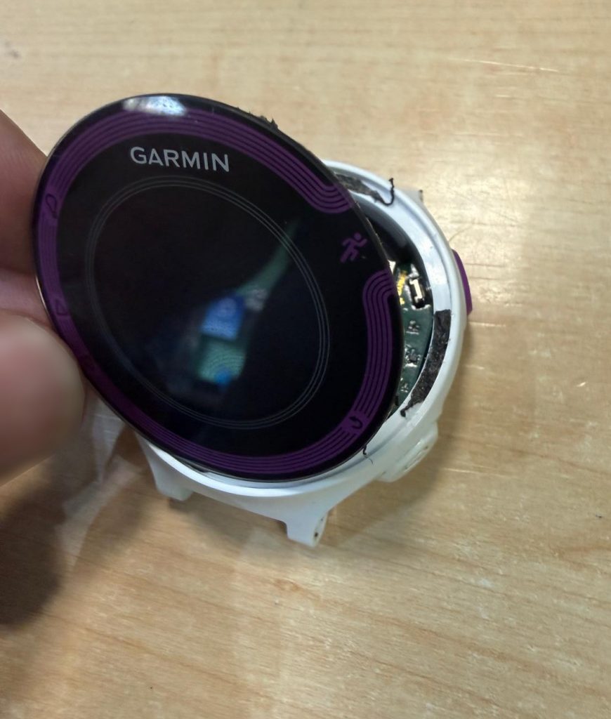 Proceso de apertura de la pantalla frontal del Garmin Forerunner 220 mostrando el adhesivo sellador.