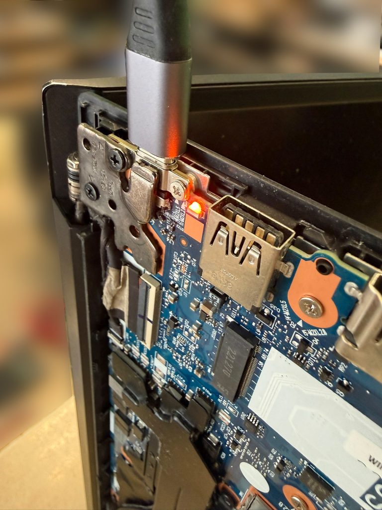 Conector USB-C conectado a la laptop con el indicador LED de carga iluminado en naranja.