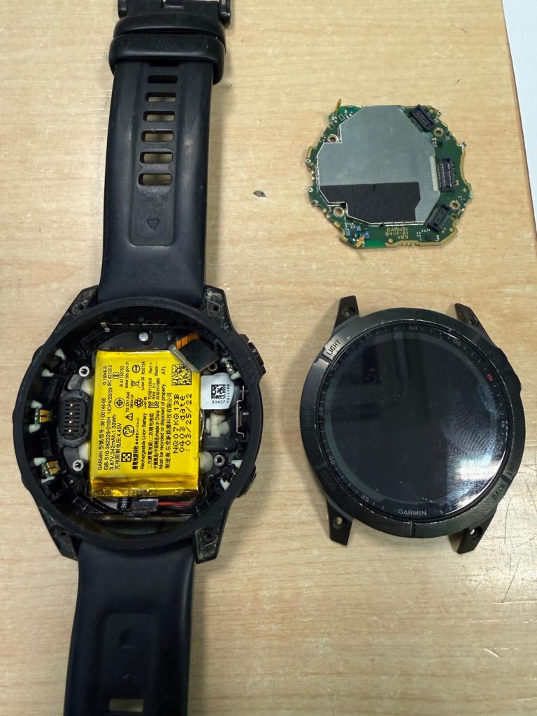 Vista de despiece del Garmin Fénix 7 Titanium mostrando la batería interna y la placa base desmontada.